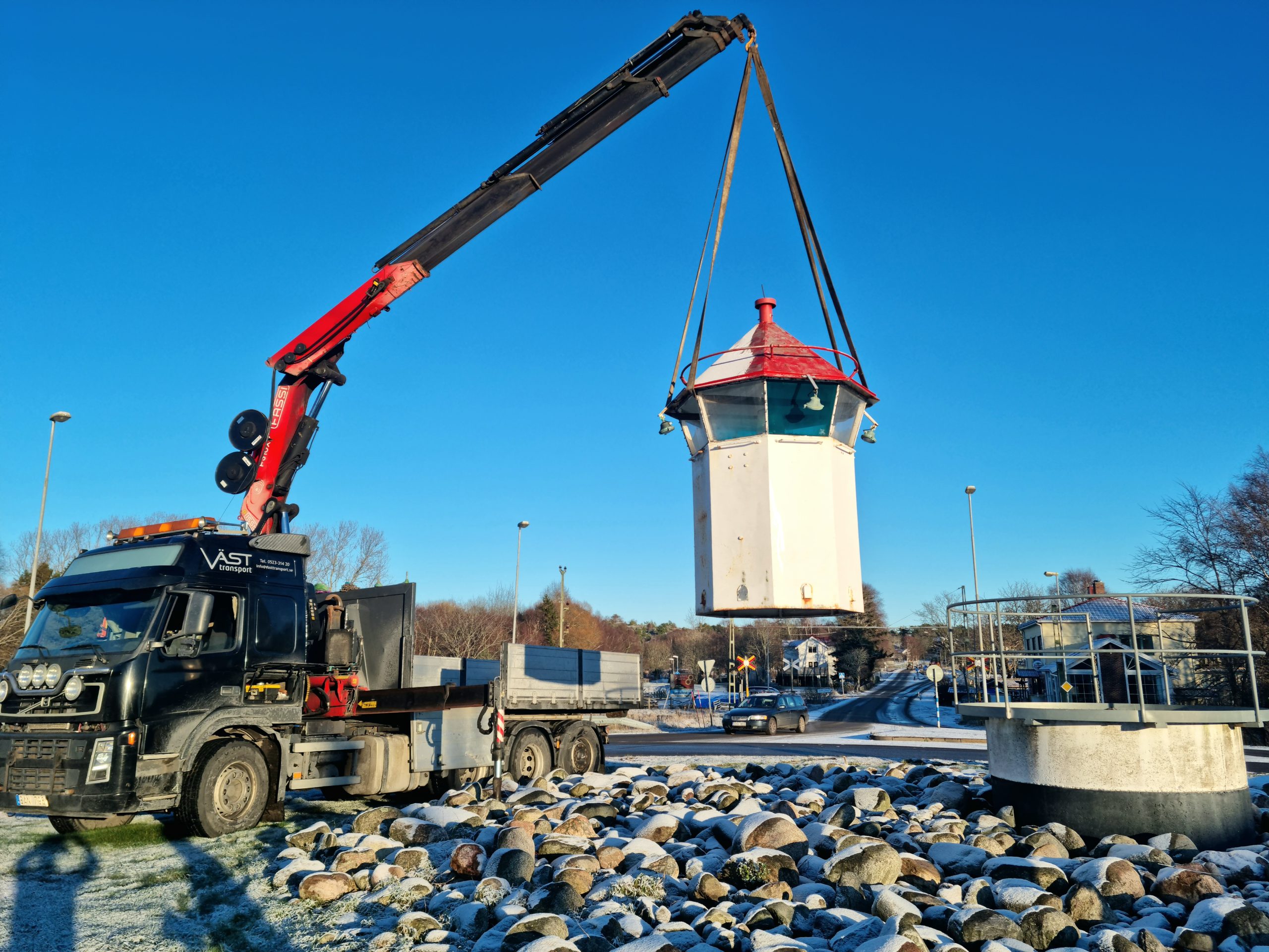 Kran monterad på lastbil lyfter ett litet hus